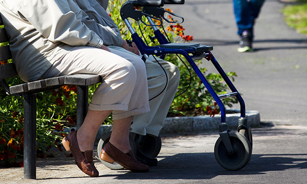 Två äldre personer med rollator som sitter på bänk i Sveaparken