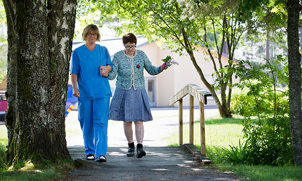 Personal och äldre kvinna på promenad utanför Järpegatans äldrebostäder