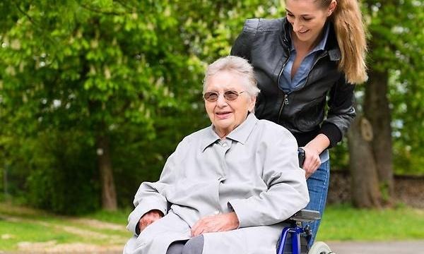Ung kvinna som hjälper äldre kvinna med rullstol